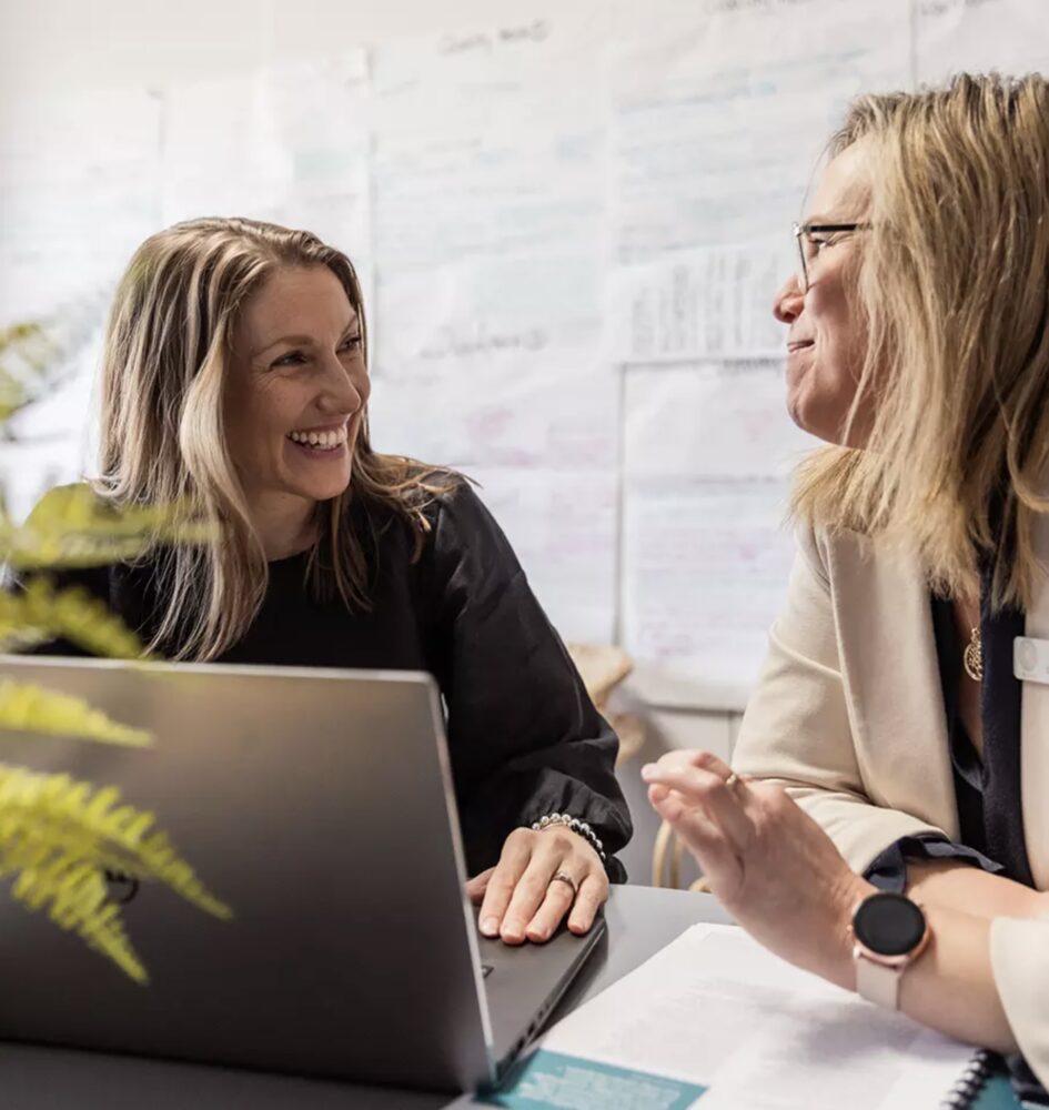 Two women laughing as they work on a laptop